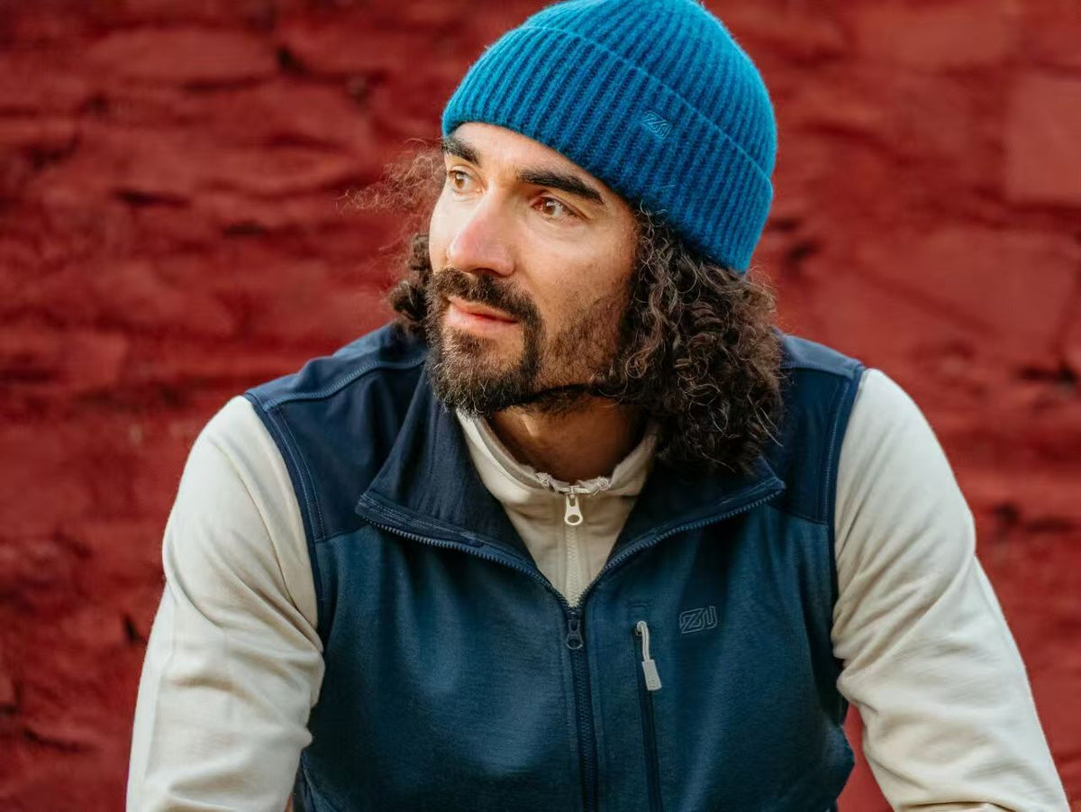 Man wearing ZEALWOOD blue merino wool beanie and fleece vest against a red stone wall