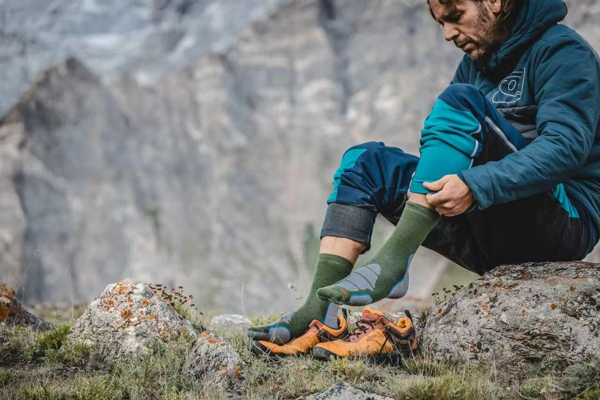 Hiker sitting on a rock changing into wool socks on a mountain trail