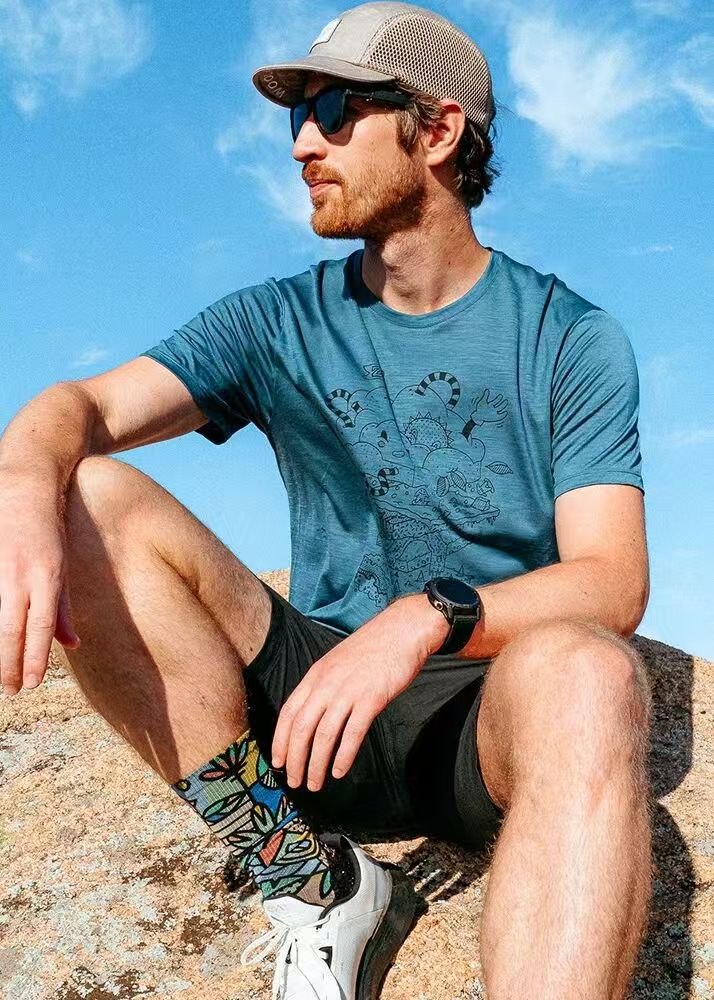 Man sitting on a rock wearing merino wool T-shirt and colorful socks on a sunny trail